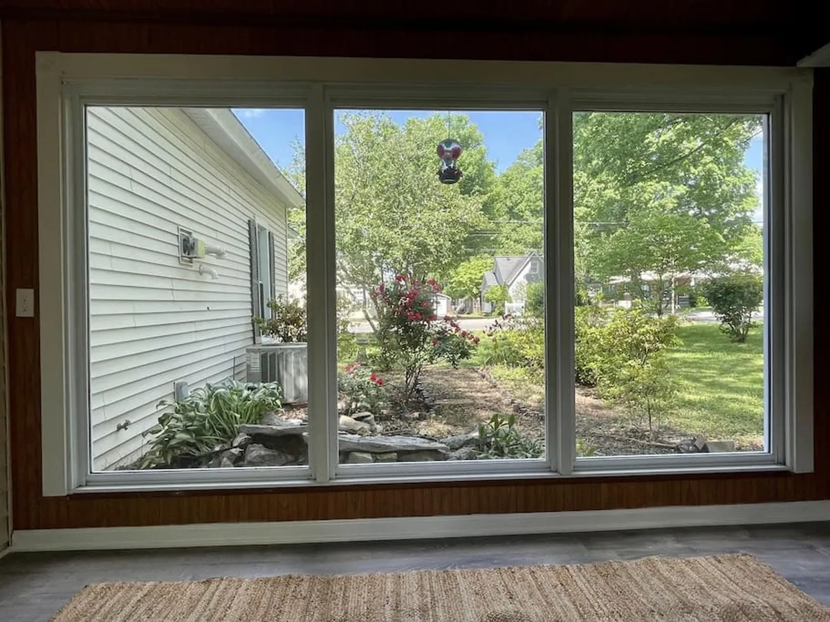A sunroom bathed in natural light, featuring large windows that offer serene views of the garden. Decorative plants and comfortable furnishings enhance the tranquil and cozy environment, making it an ideal spot for reading or relaxing.