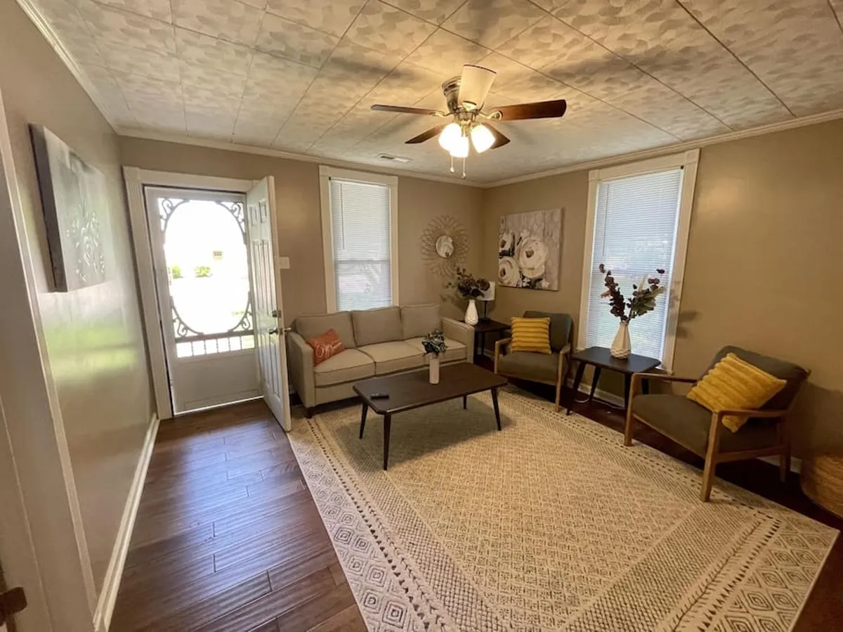 A cozy, updated living area with a comfortable sofa, decorative wall art, and a welcoming entrance, perfect for unwinding after a day of exploration. The space is set up for socializing, relaxing, and group gatherings.