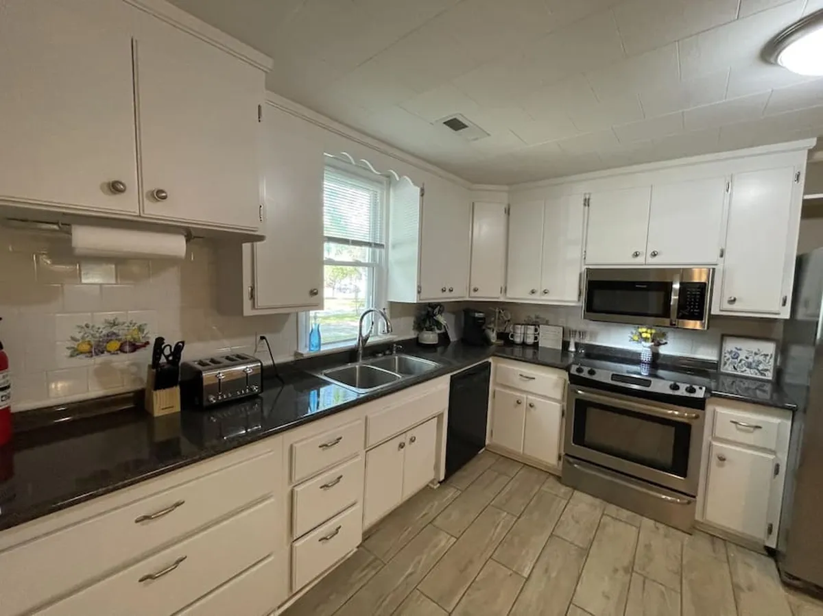 A modern kitchen space with a gleaming countertop, stainless steel appliances, a window letting in natural light, and colorful decorative touches. The kitchen is ready for meal prep, socializing, and family gatherings.
