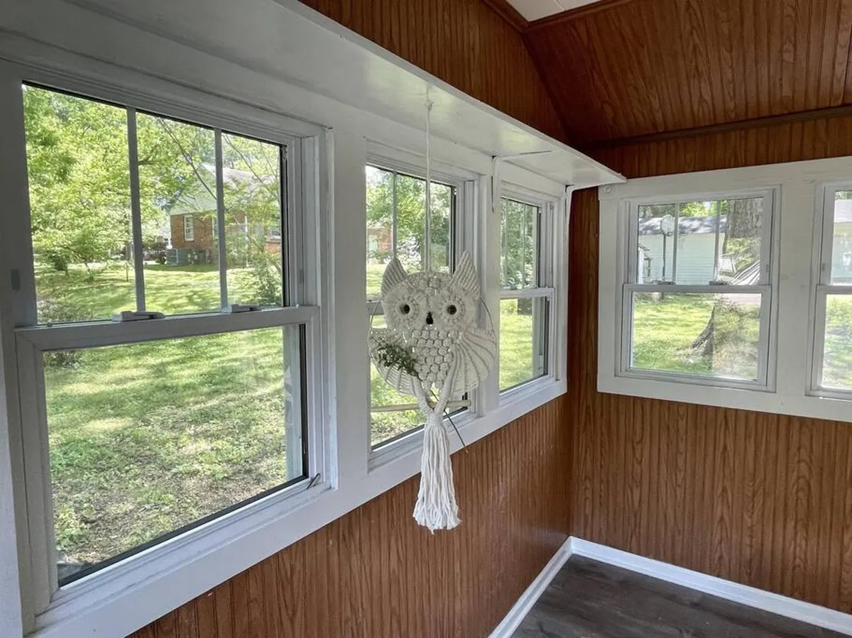 A sunlit room with large windows, wood paneling, and a charming hanging owl decoration. The seating area provides a comfortable spot to relax, gaze outside, and unwind after a day exploring. The abundance of natural light and views of the outdoors reinforce the connection between adventure and relaxation at home.
