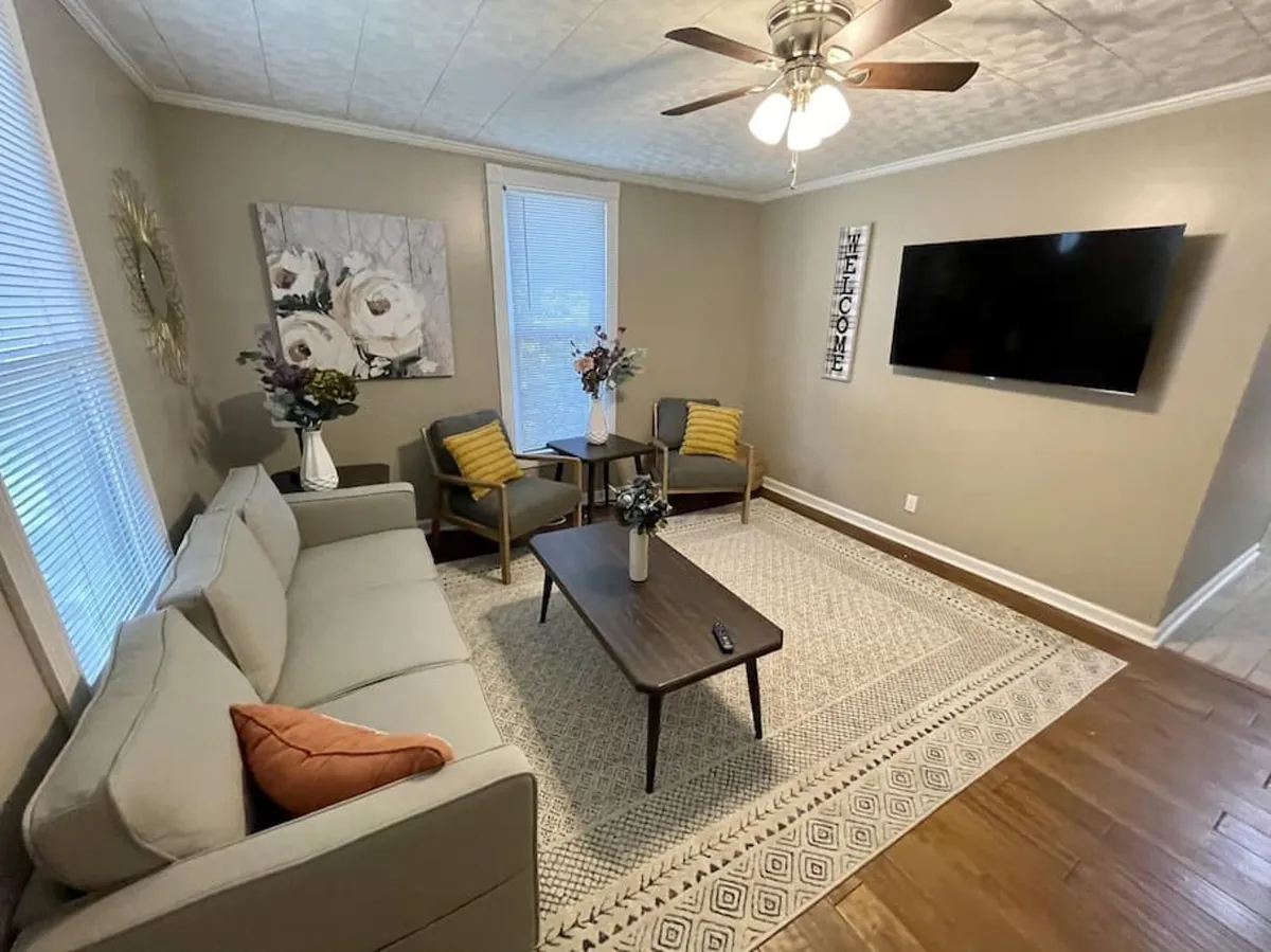 A cozy, inviting living room featuring a plush sofa, coffee table adorned with a floral arrangement, wall art, and a television. The space exudes comfort and is arranged for relaxing, socializing, and enjoying movie nights or quiet evenings.