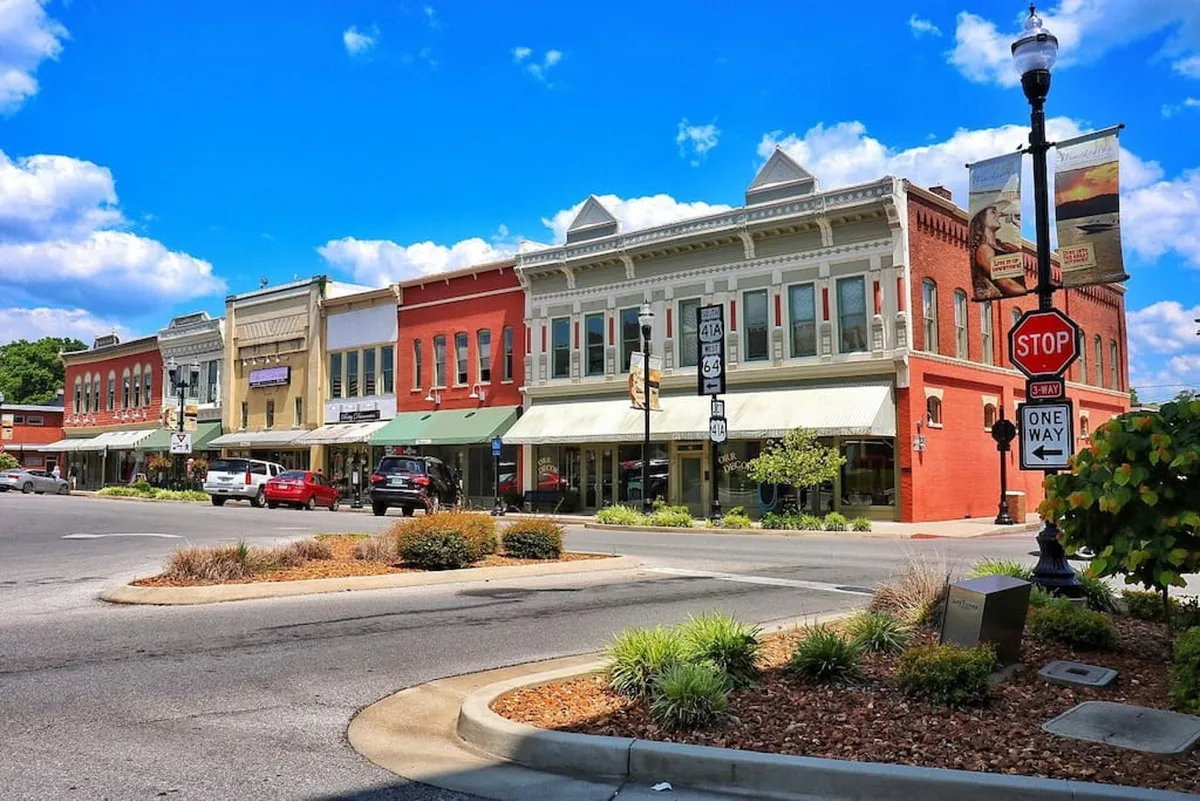 This exterior shot highlights Winchester’s vibrant historic district, featuring charming brick buildings, bustling storefronts, and lush greenery. The street scene radiates activity with visible pedestrians and a sense of community, hinting at the local shops, dining, and events accessible to visitors.